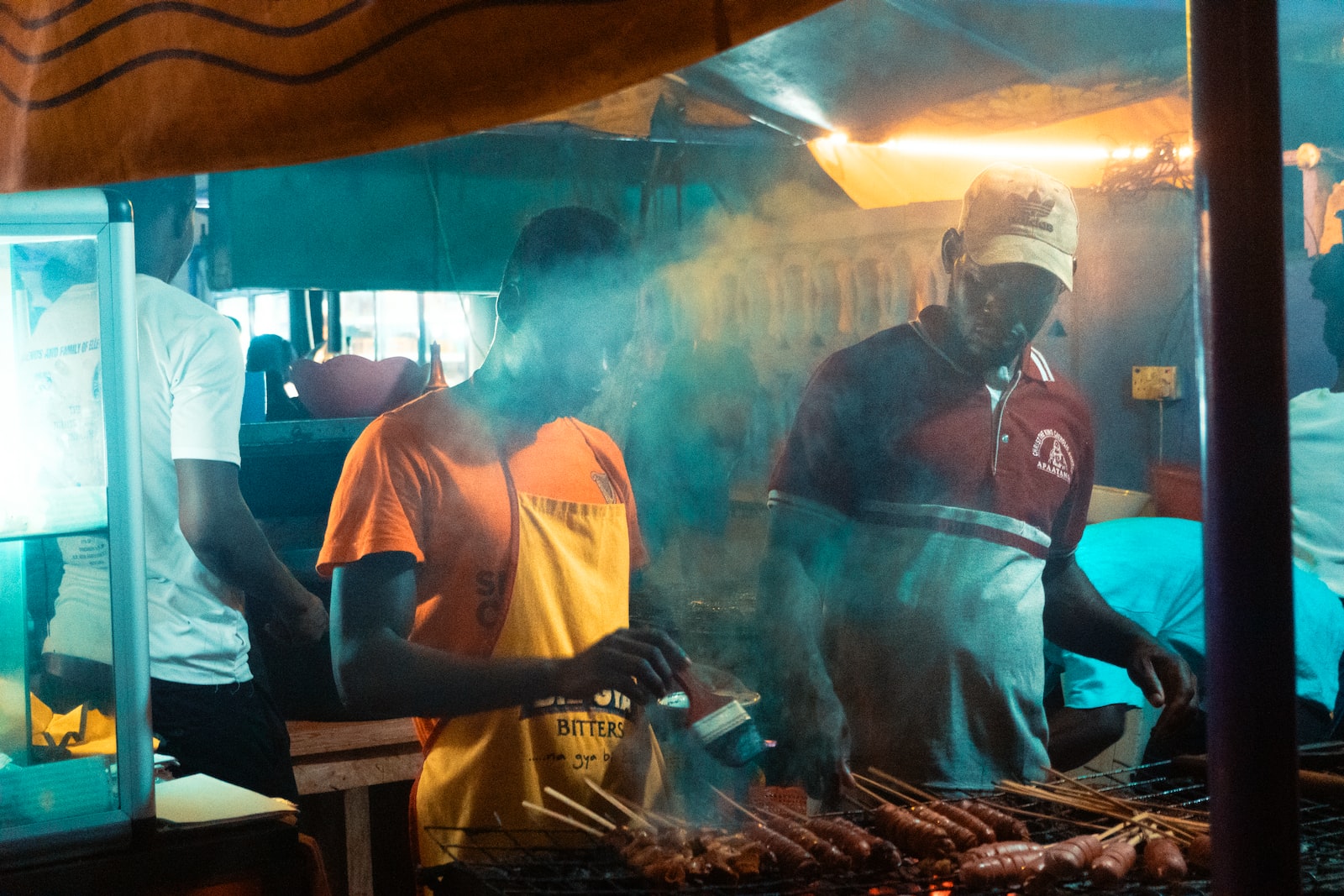 man brushes grilled skewers food beside man